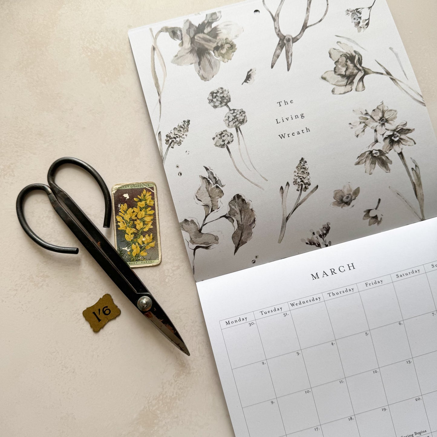 Scissors, small rectangular object with yellow flowers, and a calendar with floral design on a beige surface
