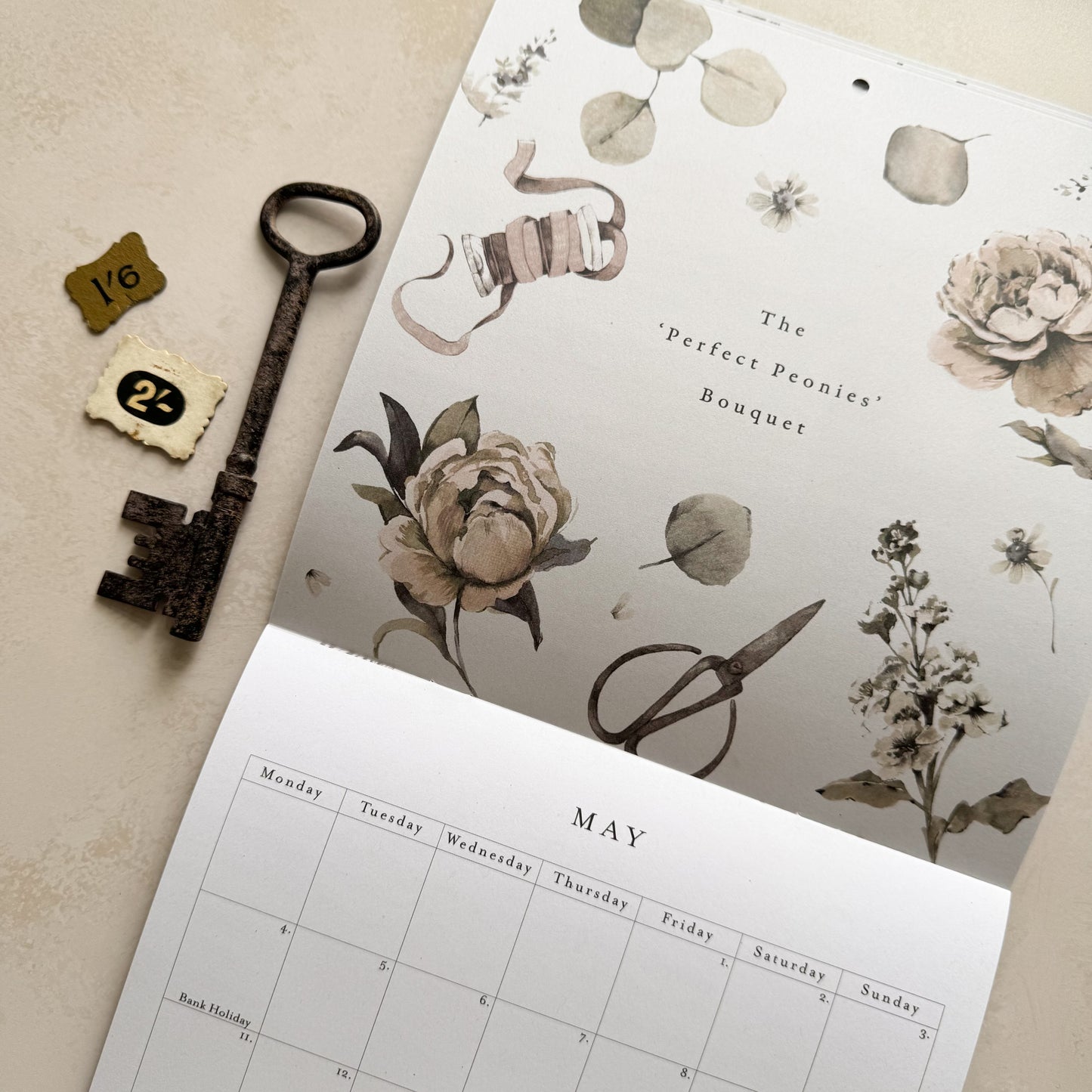 Peony floral inspired calendar for the month of may on a beige surface surrounded by a key