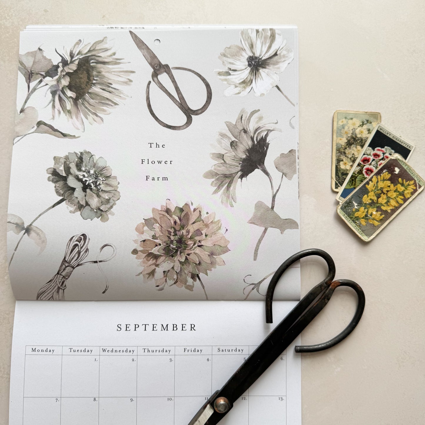 Floral-patterned calendar with scissors and small tin on a beige background