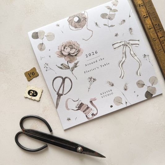 Floral design calendar with decorative elements on a beige surface with scissors and a ruler.