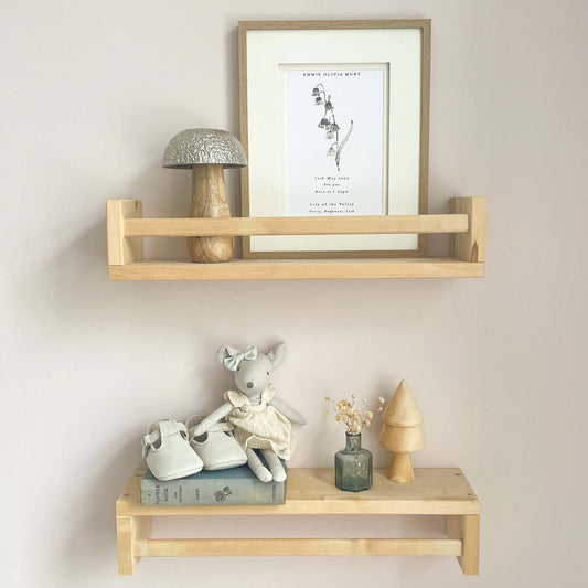 A nursery lifestyle image showing two wooden shelves with birth flower personalised baby print in a oak frame alongside baby shoes and a mouse doll.